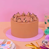 Classic Chocolate Cake by Crumbs & Doilies with smooth chocolate buttercream and chocolate chip decoration on pink background.